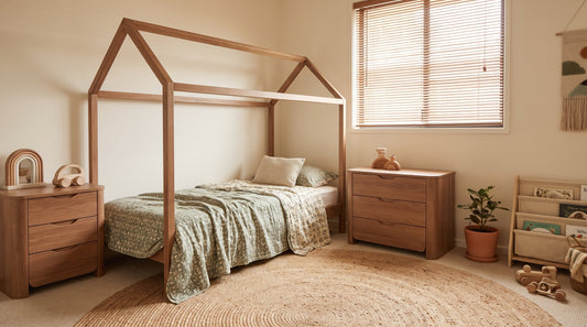 Montessori-style house-frame floor bed in a warm, neutral toddler bedroom with sage green bedding, wooden furniture, and natural light